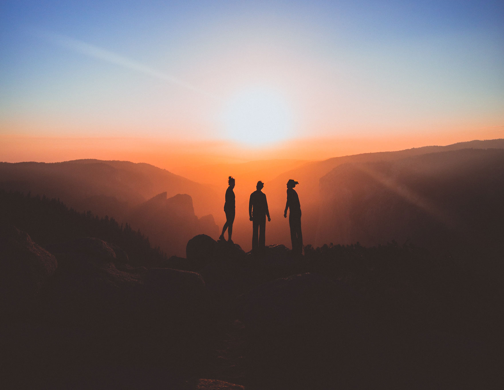 group of three on top of mountain in front of sunset