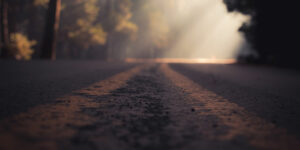 double yellow lines of shadowy road leading to ray of sunshine