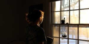 morning sun shining into dark room. Light gently illuminating face of woman pensively looking out window.